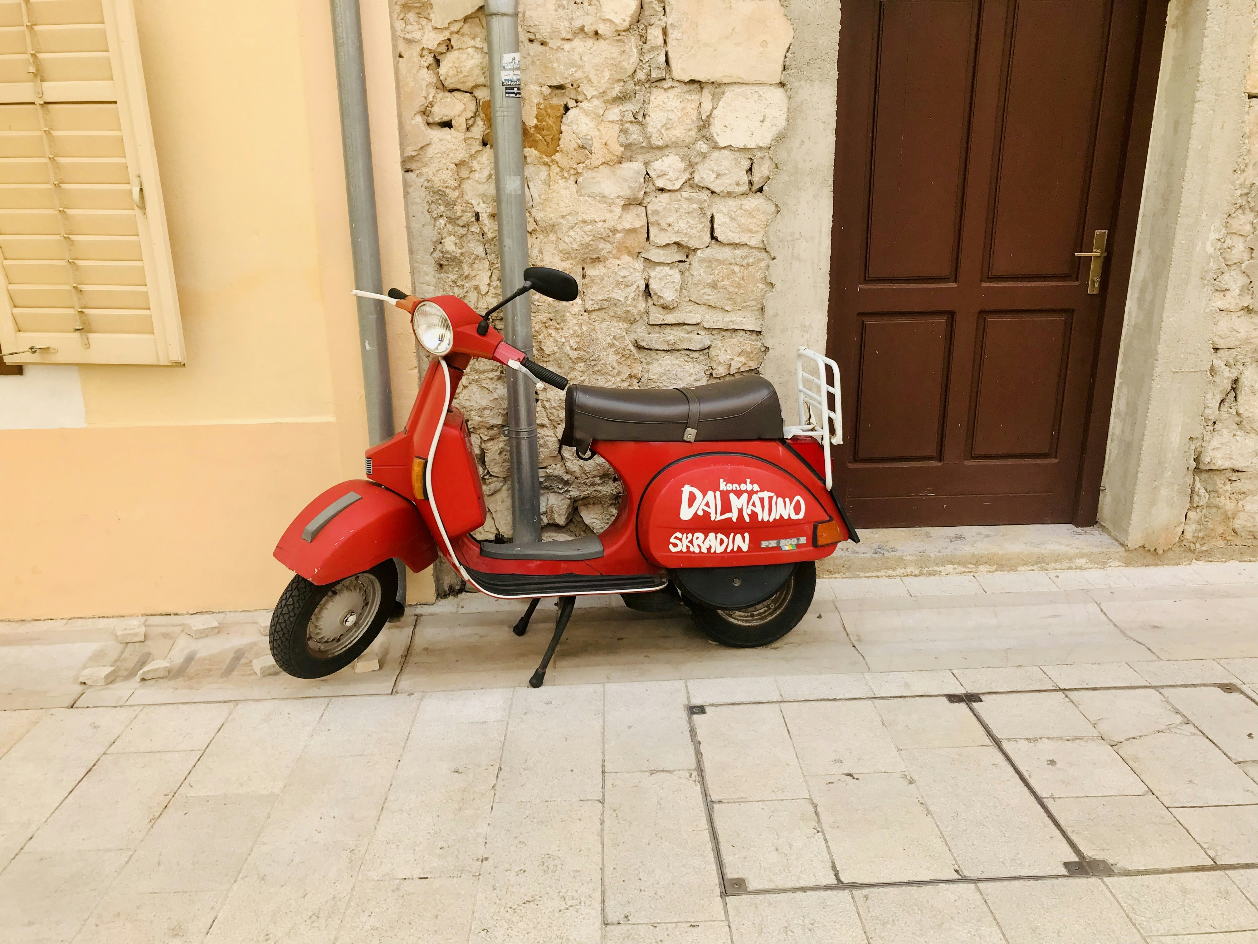 red and black motor scooter parked beside brown brick wall