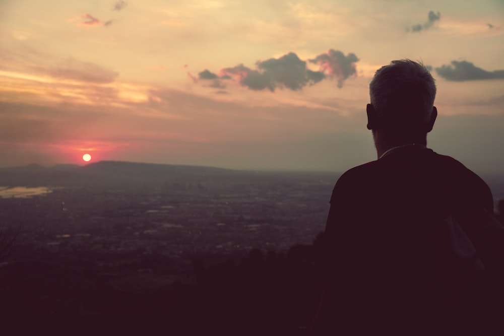 silhouette of man standing on top of mountain during sunset