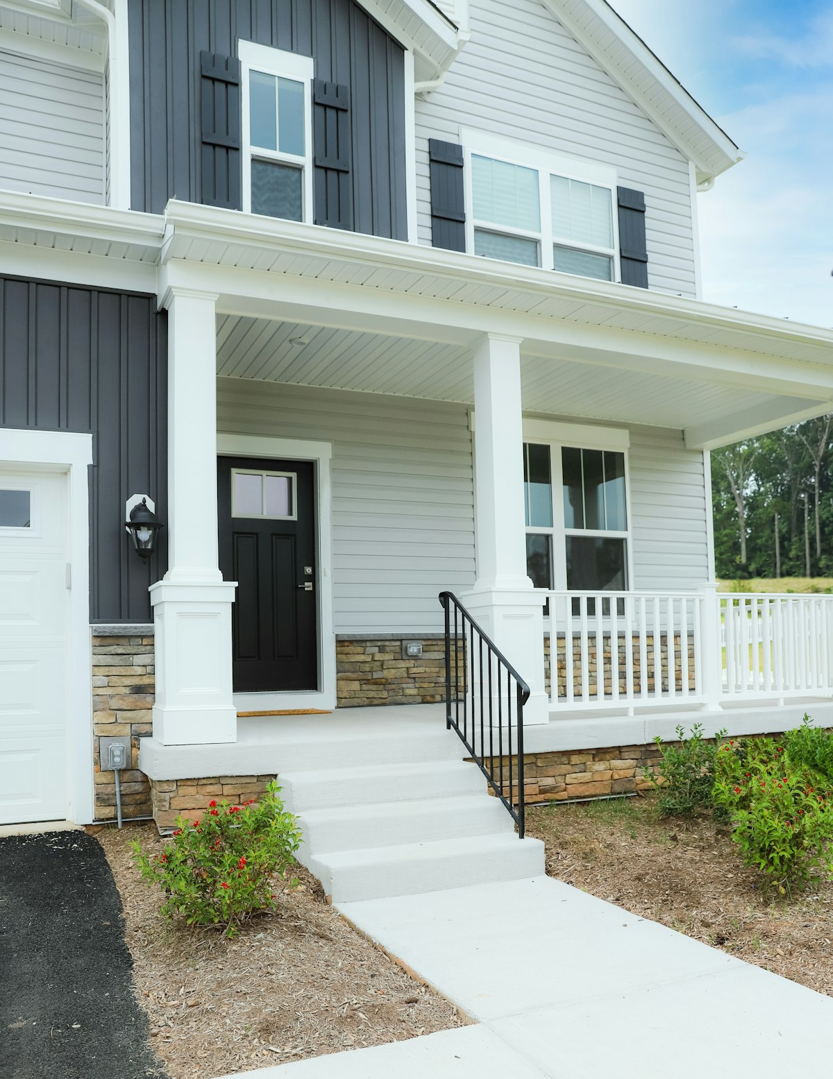 Two-story home exterior with gray siding, black shutters, and a covered porch