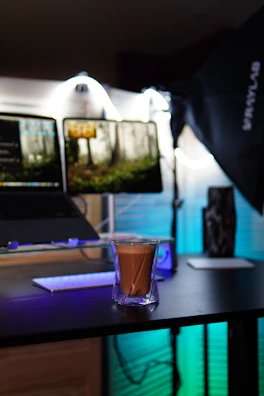 A modern home workspace with dual monitors, plants, and a cup of coffee, bathed in natural light.
