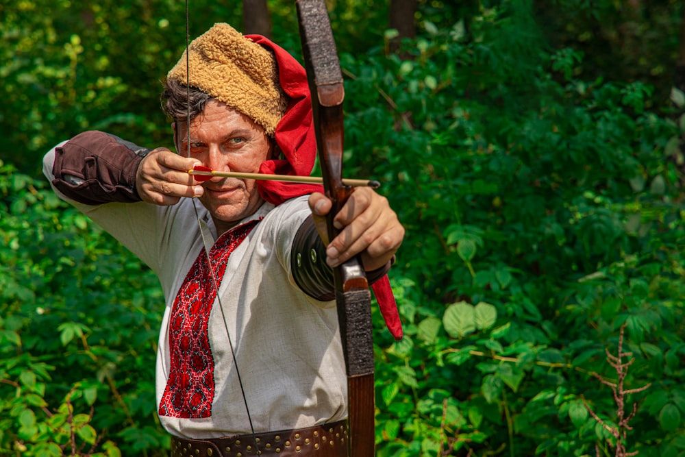 man in white shirt holding bow and arrow