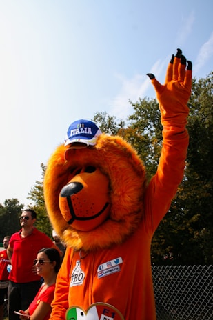 A vibrant mascot costume of a cheerful lion made from plush and foam, standing in a sunny park.