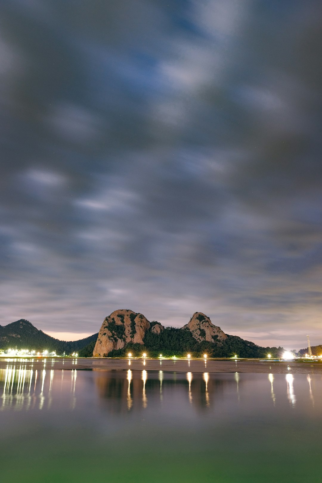 body of water near mountain under cloudy sky during daytime