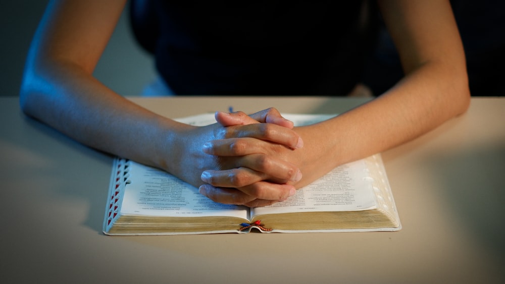 a person sitting at a table with their hands folded over a book