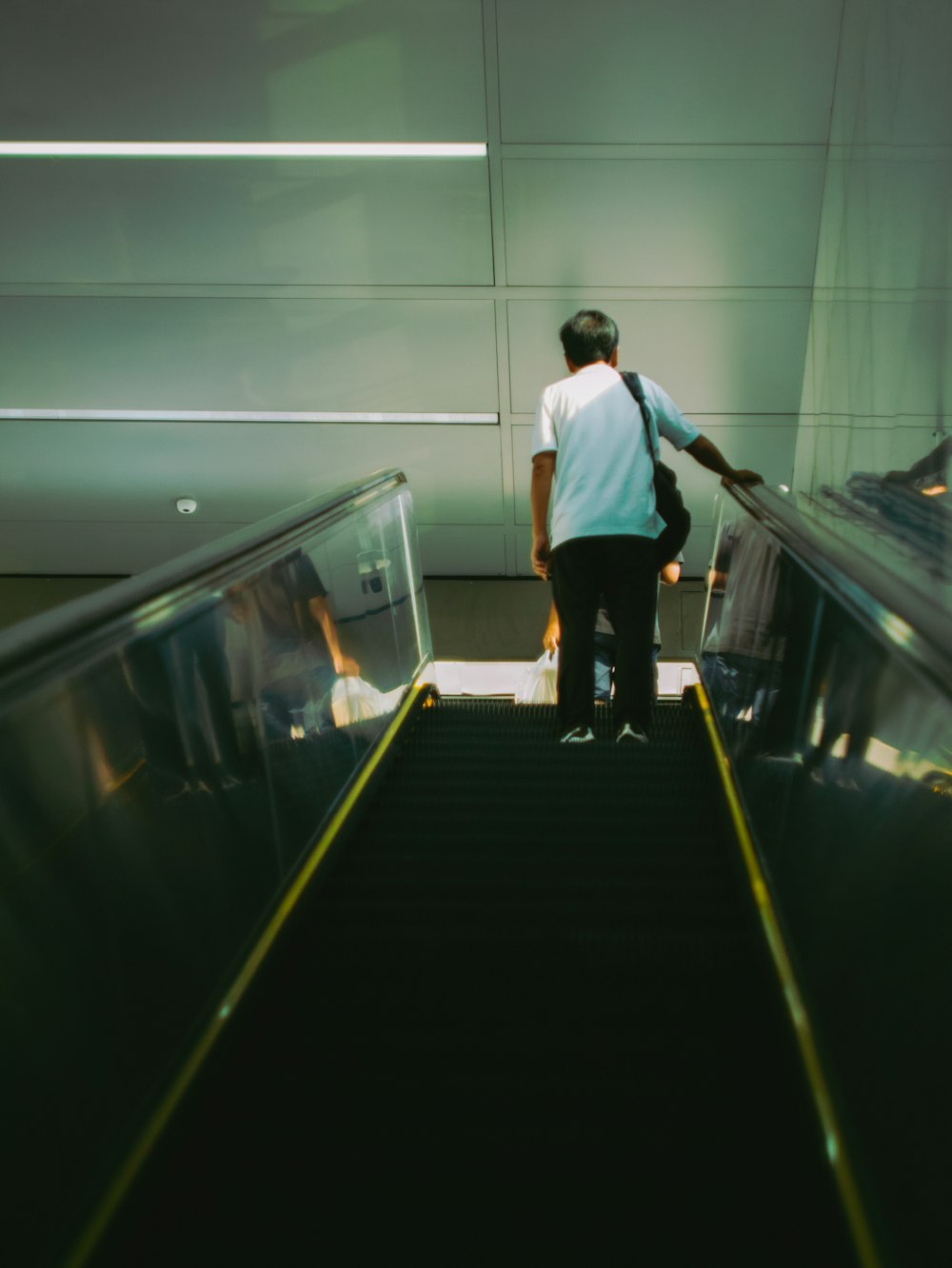 man in white shirt and black pants walking on escalator