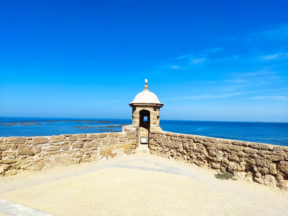 a stone wall next to the ocean with a bell tower