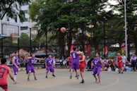 A sunlit outdoor court with players in action, purple jerseys contrasting against a clear blue day.