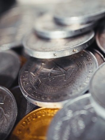 A close-up view of a pile of coins, primarily metallic in appearance with distinct engravings and details visible on the surface.
