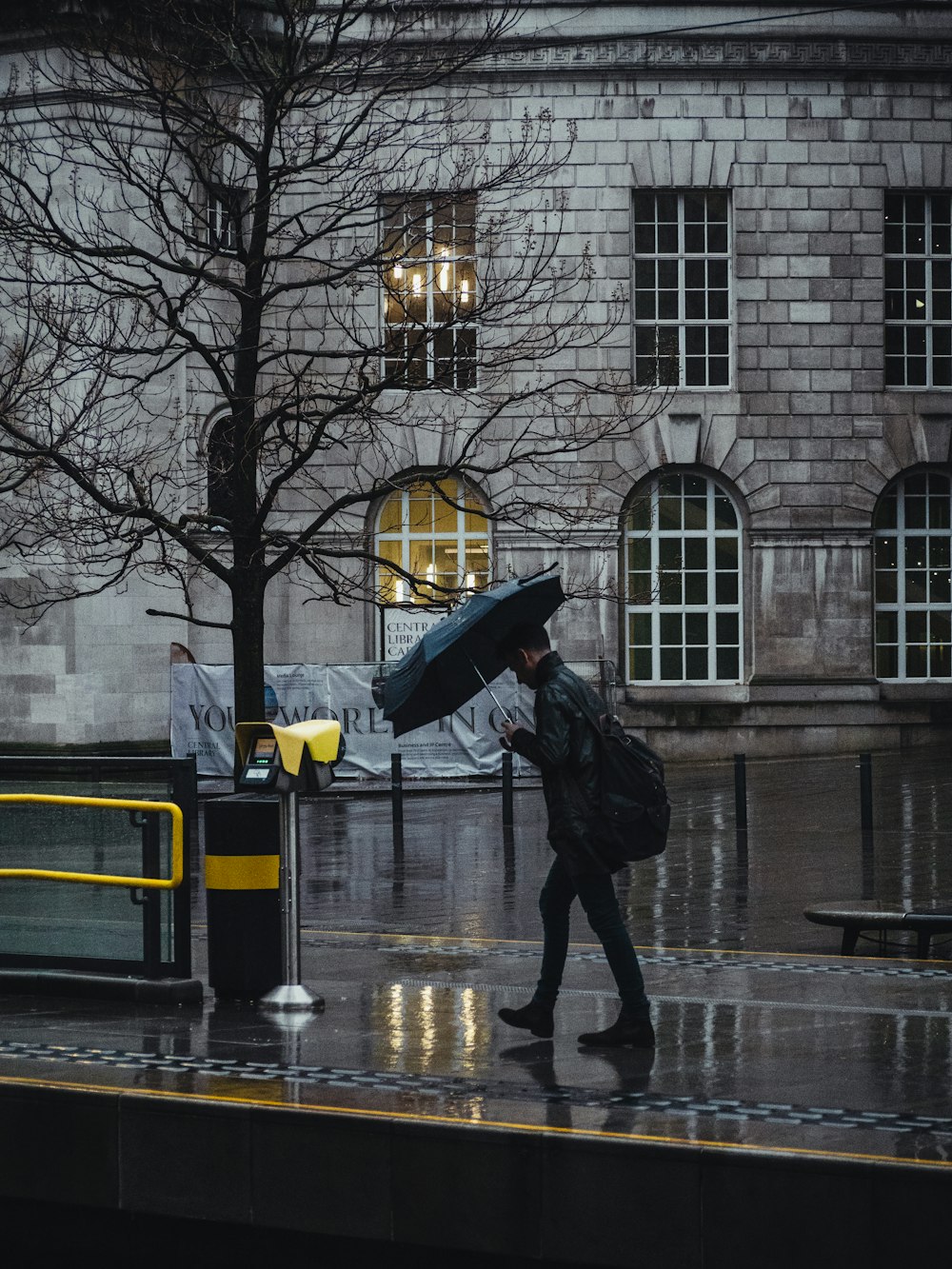 person in black jacket and black pants holding umbrella walking on sidewalk during daytime