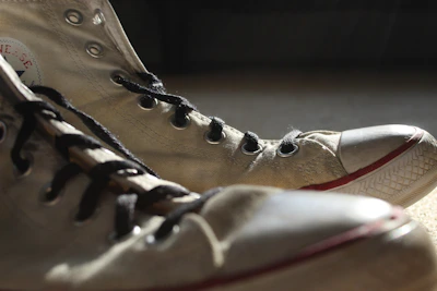A close-up of a pair of well-worn vintage sneakers resting on a wooden floor, sunlight casting warm tones.