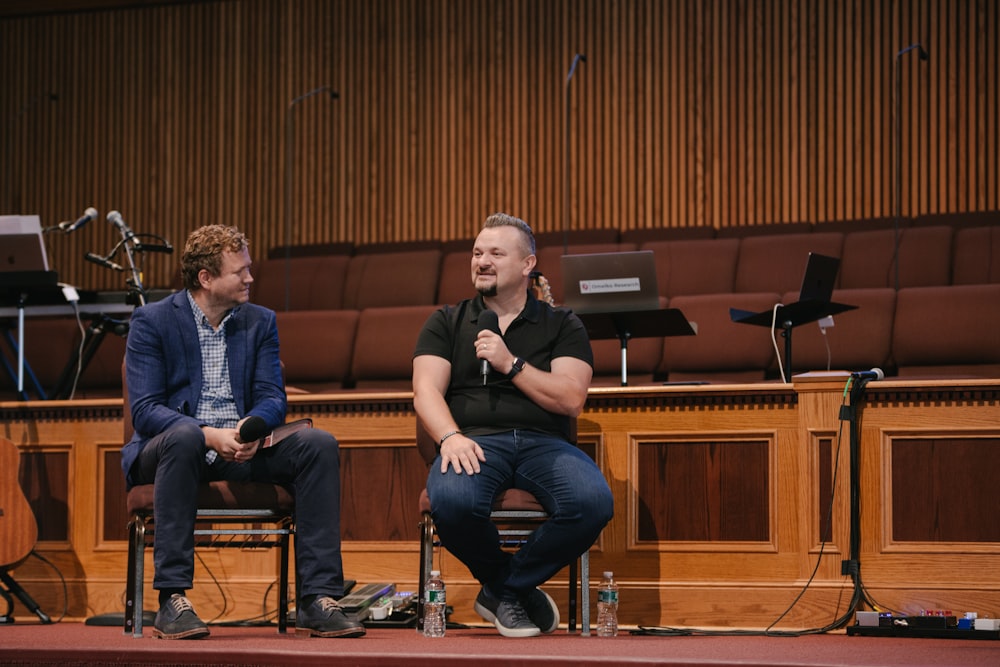 two men sitting on chairs in front of a stage