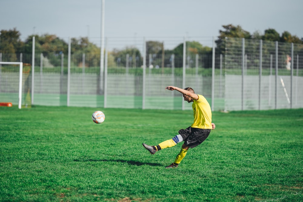 Hombre con camisa amarilla y pantalones cortos negros jugando al fútbol durante el día