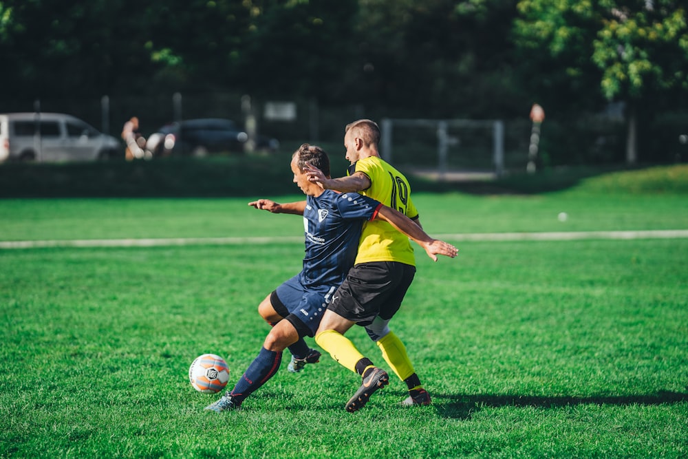 boy in blue and yellow soccer jersey kicking soccer ball on green grass field during daytime