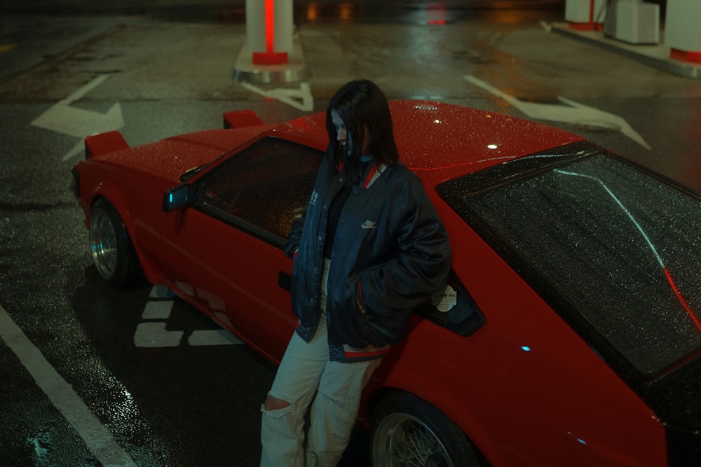 man in black jacket standing beside red car