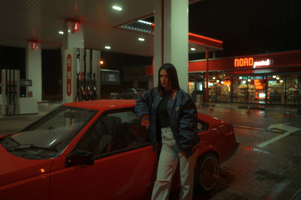 man in black jacket standing beside red car