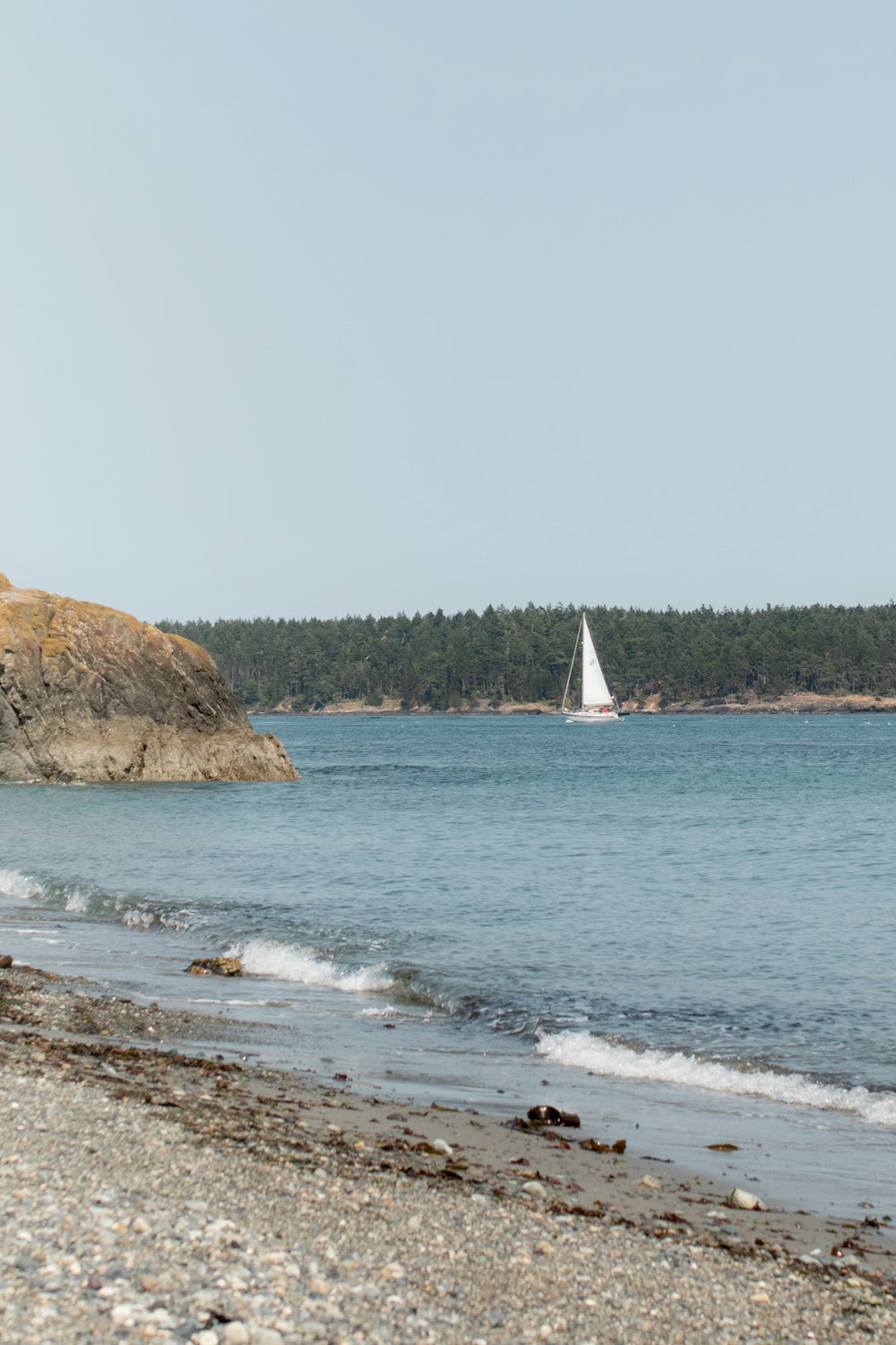 a sailboat on the water near a rocky shore