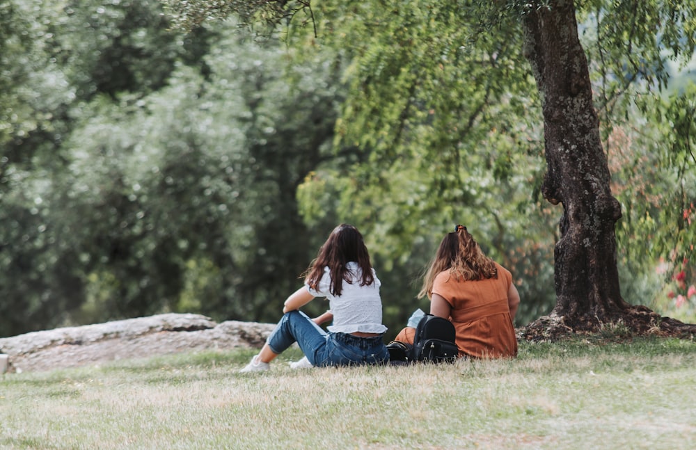 a couple of women sitting on top of a grass covered field