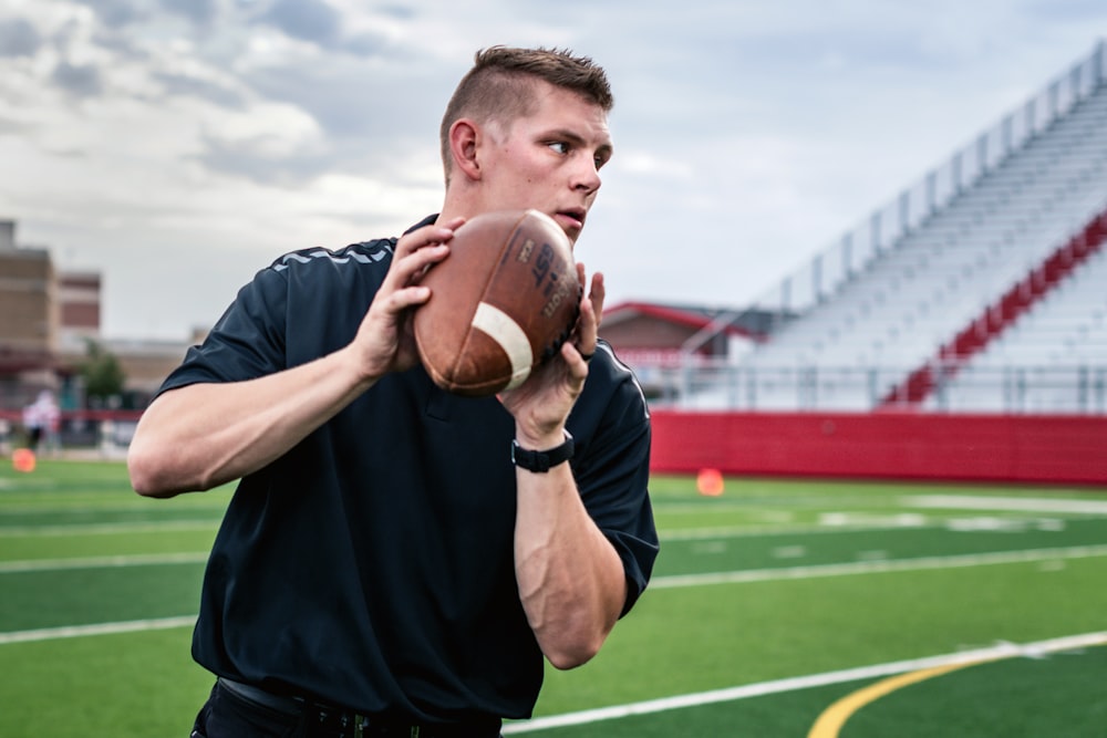 man in black crew neck t-shirt holding brown football