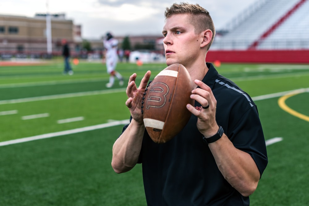 man in black crew neck t-shirt holding brown football