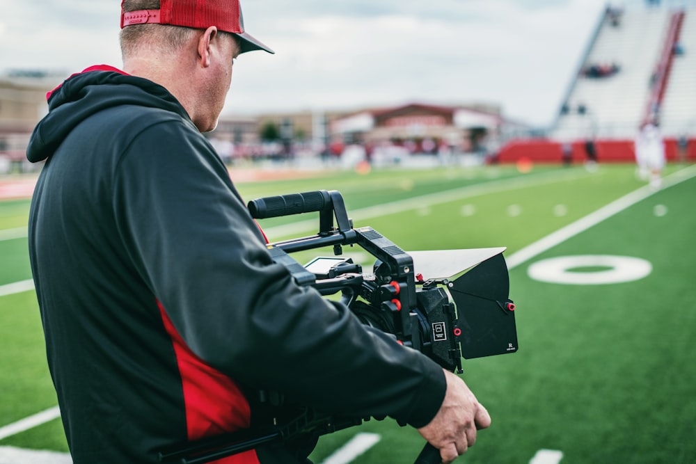 man in black and red long sleeve shirt holding black video camera during daytime