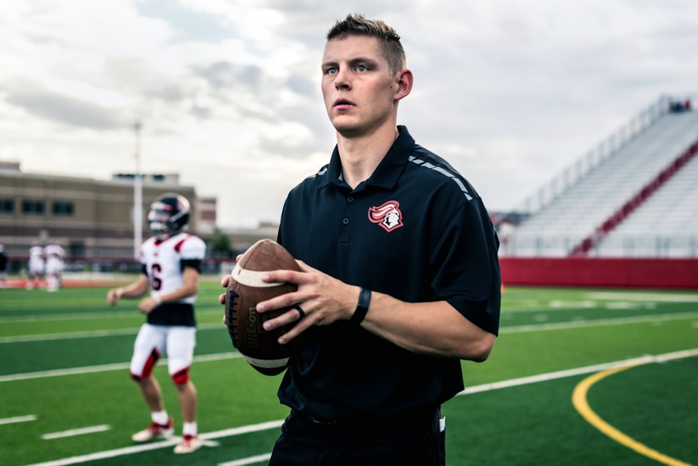 man in black polo shirt holding brown football