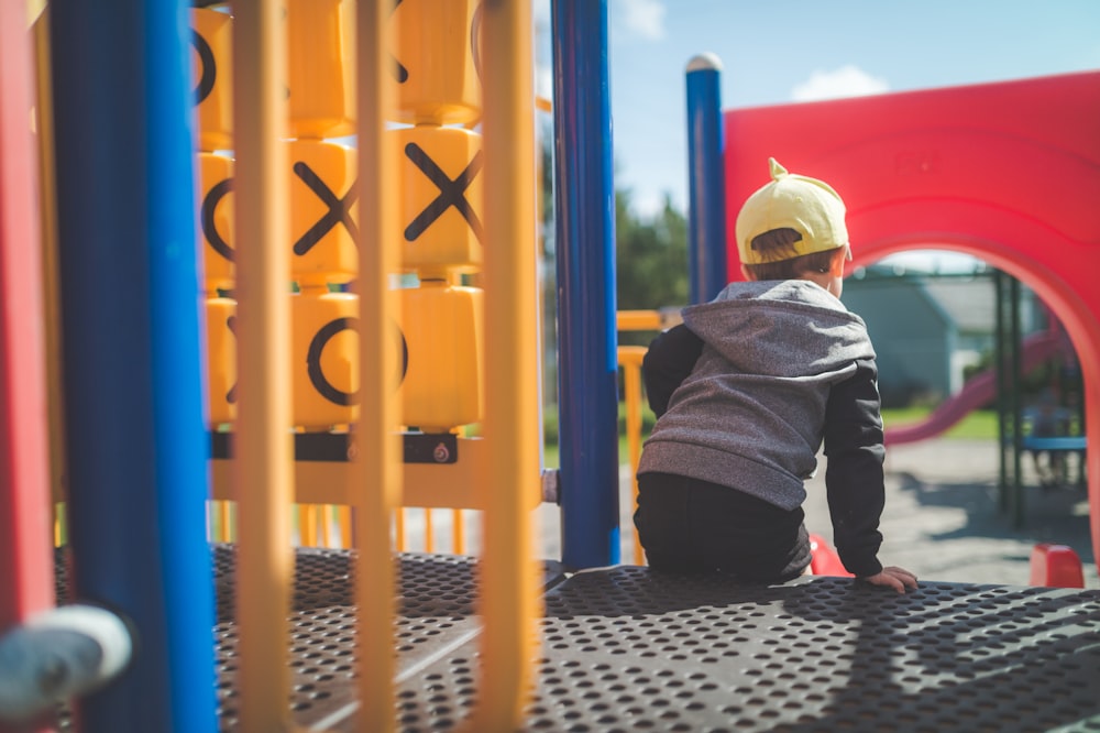 boy in black and gray hoodie sitting on yellow metal playground during daytime