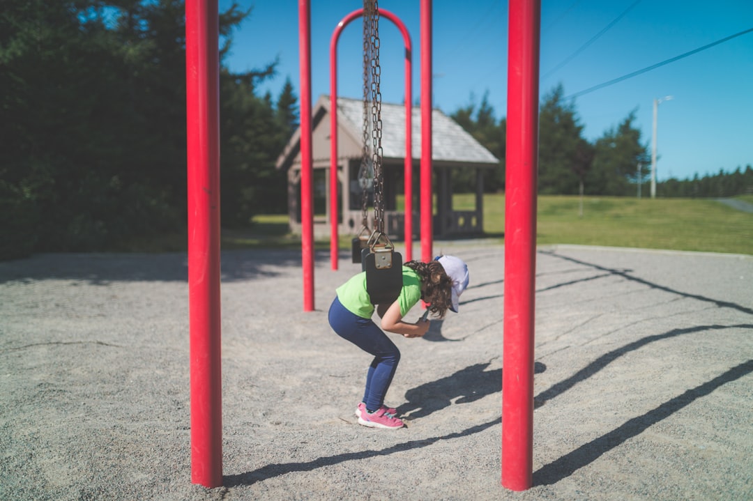 girl in blue jacket and blue denim jeans playing on red and blue metal bar during