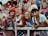 A group of young adults, mostly women, dressed in patriotic-themed clothing and face paint, standing behind a metal fence at what appears to be a sporting or public event. One wears a red hat with text and another is wearing an eagle hat. They are smiling and appear to be enjoying the event.