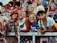 A group of young adults, mostly women, dressed in patriotic-themed clothing and face paint, standing behind a metal fence at what appears to be a sporting or public event. One wears a red hat with text and another is wearing an eagle hat. They are smiling and appear to be enjoying the event.