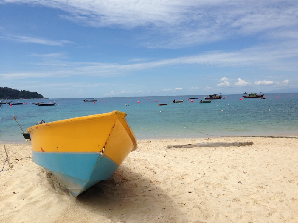 a yellow and blue boat sitting on top of a sandy beach