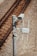 A surveillance camera is mounted on a metal pole beside railway tracks. The pole also has attached electronic equipment with antennas, likely for communication or data transmission. The tracks run parallel on gravel-covered ground.