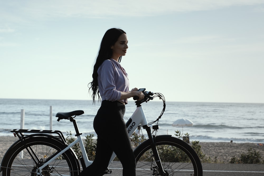 Mujer con camisa blanca y pantalones negros montando en bicicleta cerca del cuerpo de agua durante el día