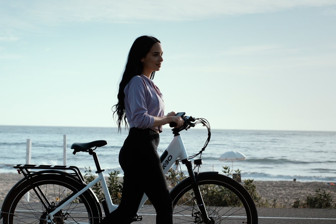 woman in white shirt and black pants riding on bicycle near body of water during daytime