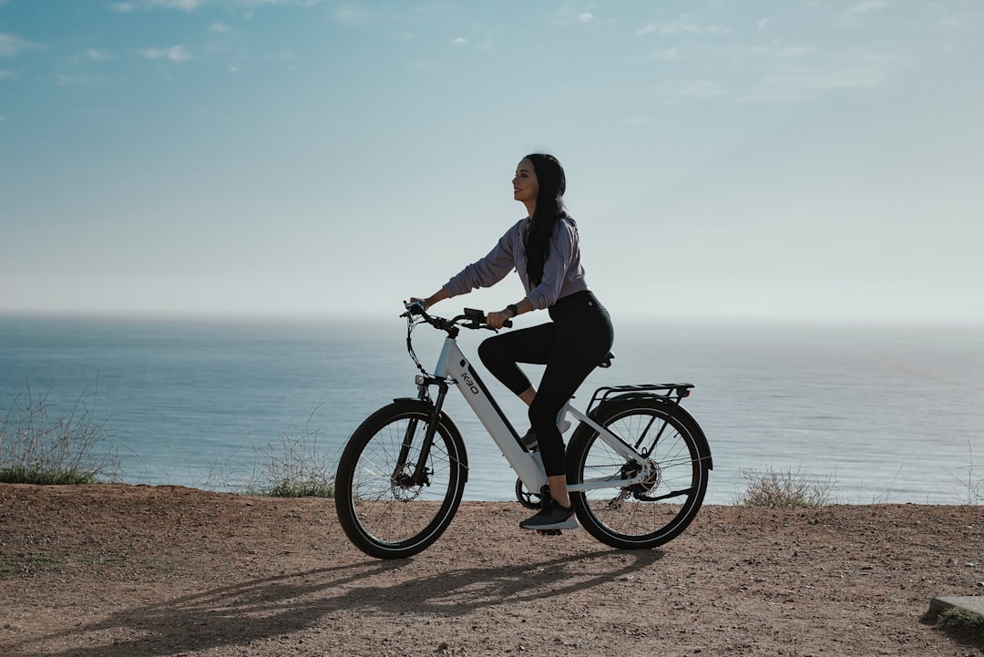 man in black jacket riding on black bicycle near sea during daytime