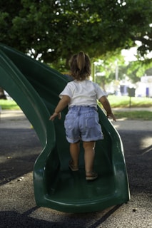 a little girl playing on a green slide