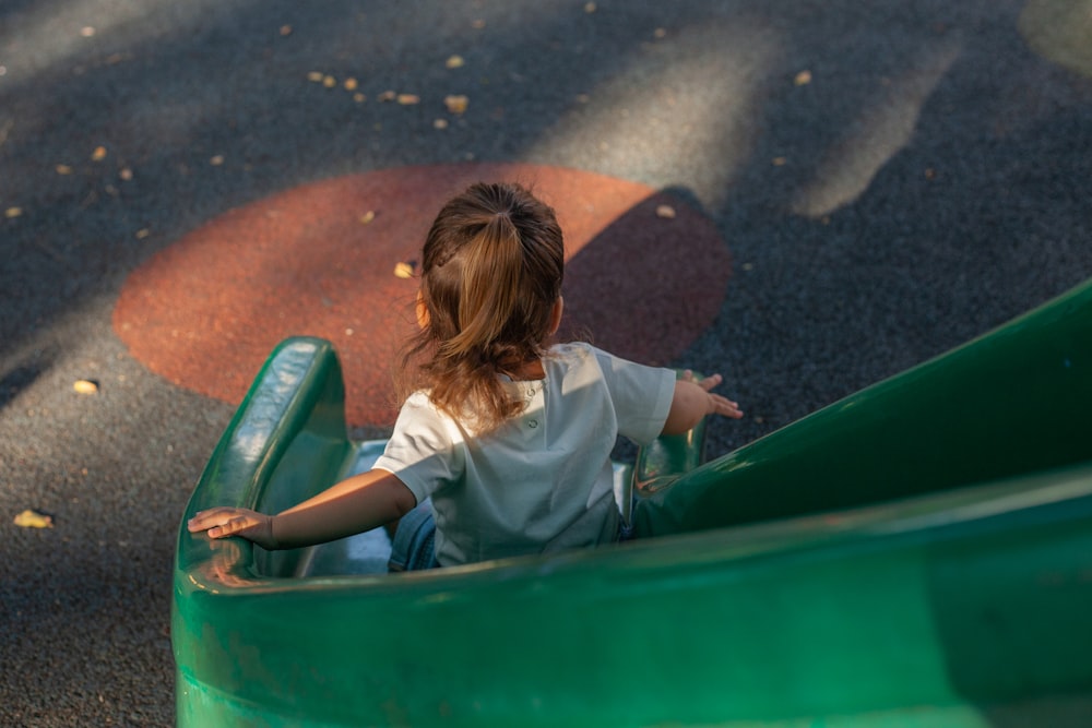 a little girl riding on a green slide