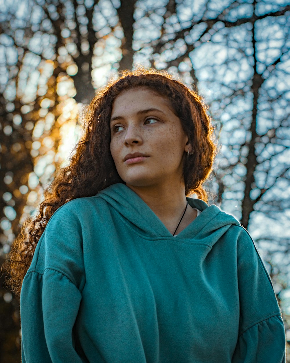 a woman in a green hoodie standing in front of trees