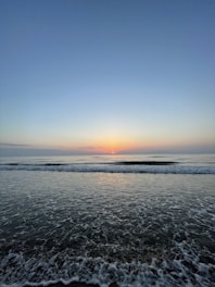 Window view from a hotel room showing a calm ocean at sunrise.