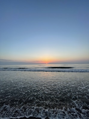 A serene early morning view of Bali’s coastline with soft golden light reflecting on calm ocean waters.