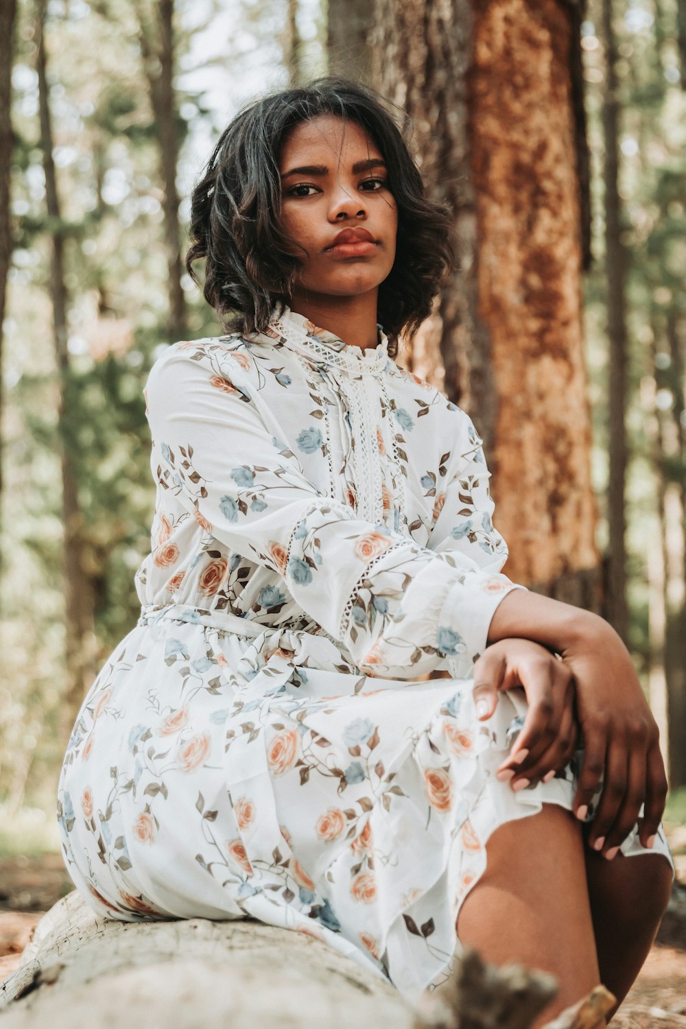 woman in white and brown floral dress sitting on brown tree trunk