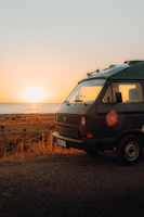 White VW T5 California Beach camper parked by a lakeside at sunset.