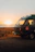 Couple enjoying a sunset picnic beside a campervan parked near a beach.