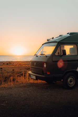 White VW T5 California Beach camper parked by a lakeside at sunset.