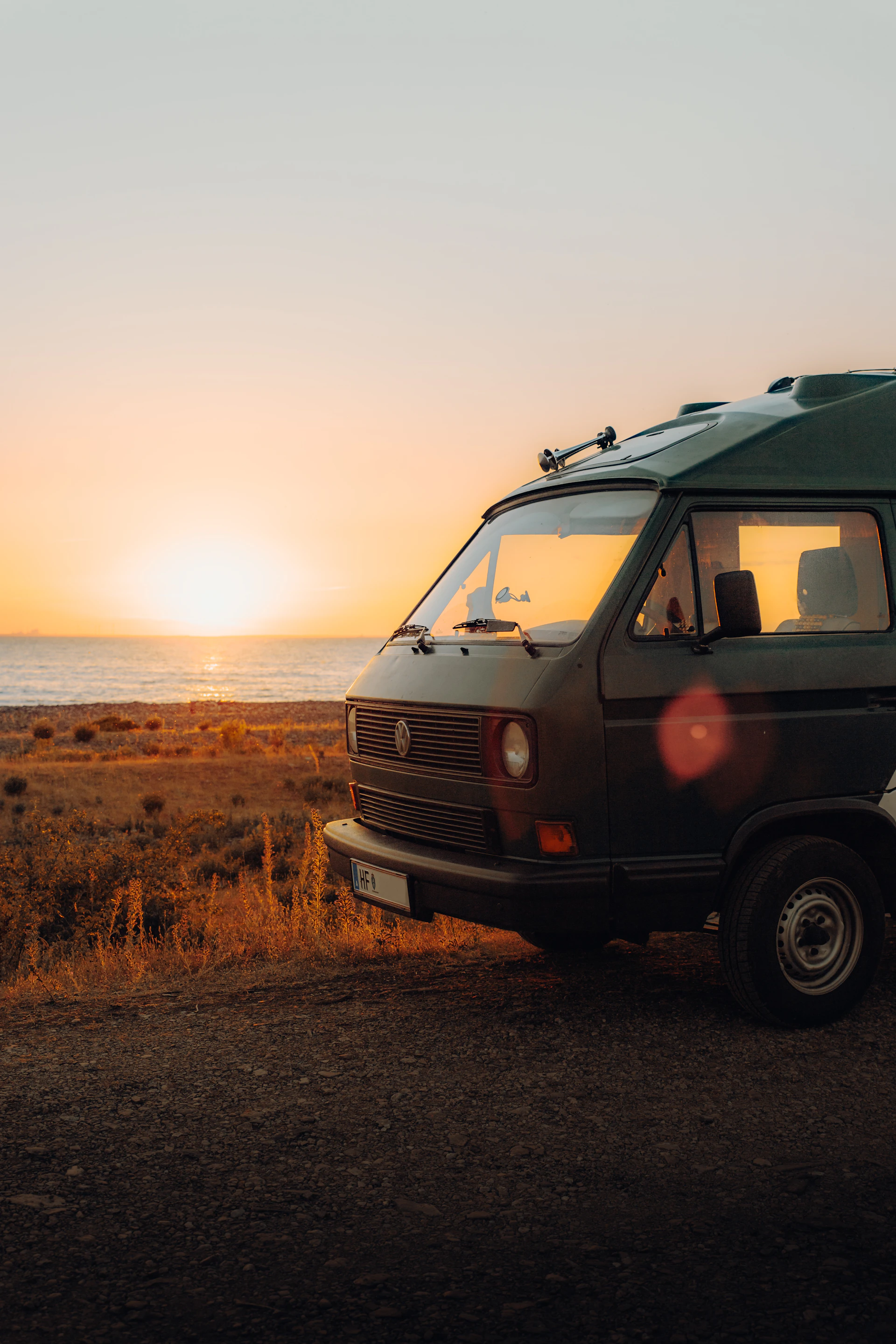 A vibrant sunset over a serene beach with a colorful kombi van parked nearby, capturing the essence of travel and freedom.