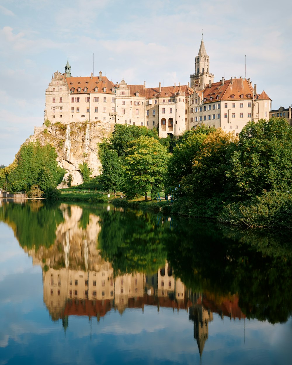 edificio in cemento marrone vicino agli alberi verdi e al lago durante il giorno