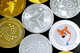 A collection of various cryptocurrency coins featuring different designs and logos. Some coins are gold, while others are silver, each with distinct symbols relating to their respective cryptocurrencies. There is a prominently displayed face of a Shiba Inu on one of the silver coins, reflecting the Shiba Inu cryptocurrency.