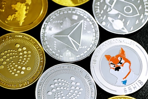 A collection of various cryptocurrency coins featuring different designs and logos. Some coins are gold, while others are silver, each with distinct symbols relating to their respective cryptocurrencies. There is a prominently displayed face of a Shiba Inu on one of the silver coins, reflecting the Shiba Inu cryptocurrency.
