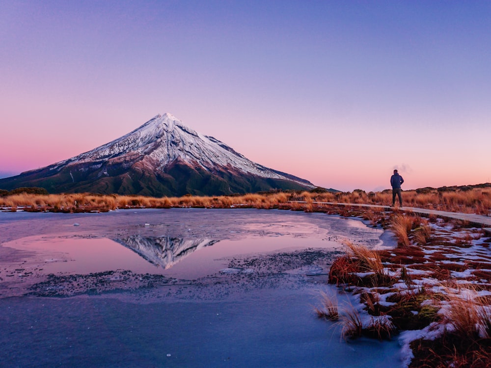 a person standing on a path near a body of water with a mountain in the