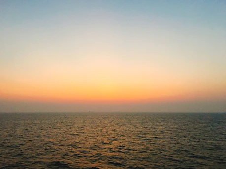 A serene ocean horizon at dawn with soft golden light reflecting on calm waters, framed by minimalist architectural lines.