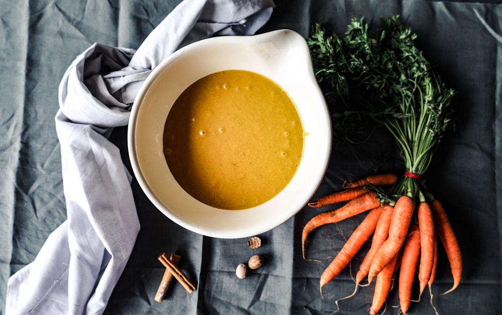a bowl of soup next to carrots and garlic